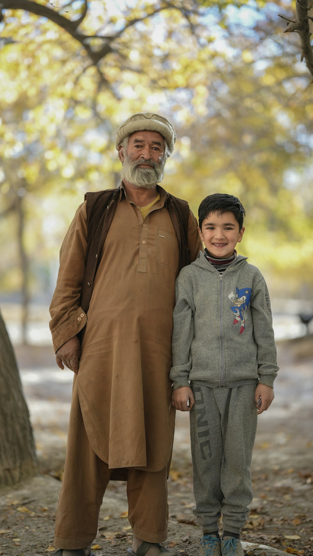 Elderly man in traditional dress standing with a young boy in a park