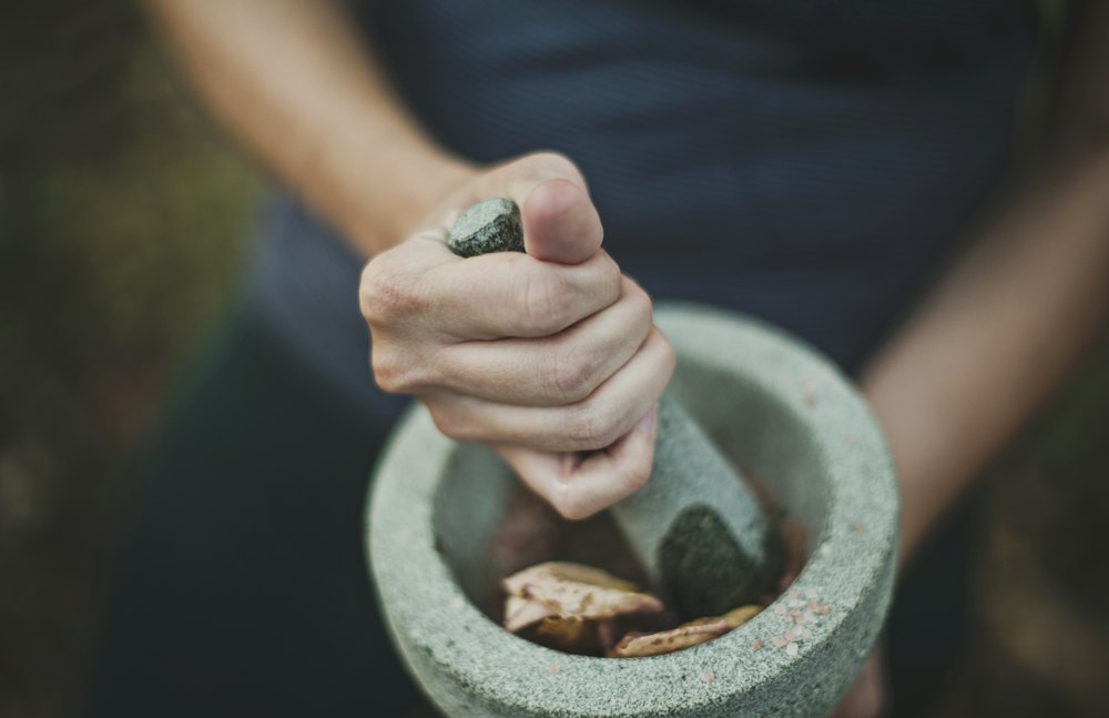 Hands grinding natural ingredients in a stone mortar and pestle